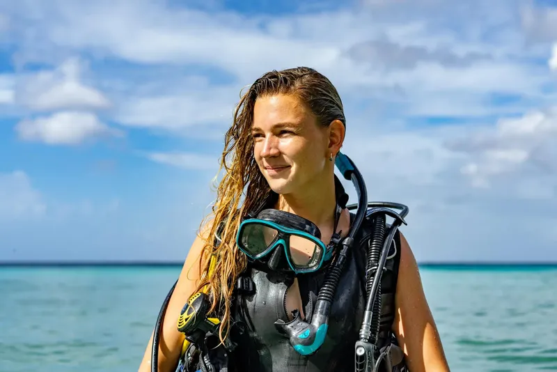 Jeune femme plongeuse souriante avec son équipement complet au bord de l'eau