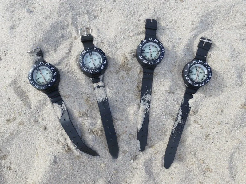 Quatre ordinateurs de plongée noirs sur du sable clair