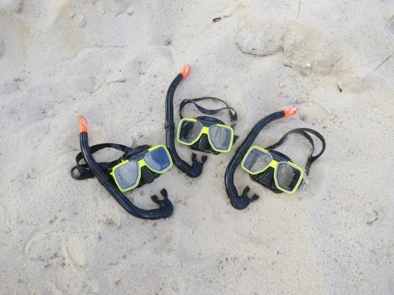 Trois masques et tubas de plongée posés sur du sable clair