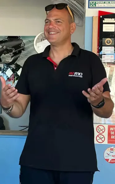 Homme souriant, instructeur de plongée, devant du matériel et affiches