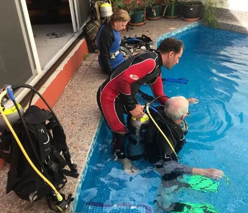 Trois plongeurs en combinaison près d'une piscine avec du matériel