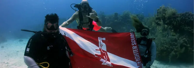 Trois plongeurs sourient et tiennent un drapeau de centre de plongée