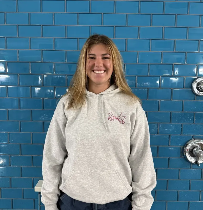 Jeune femme souriante portant un sweat à capuche devant un mur carrelé
