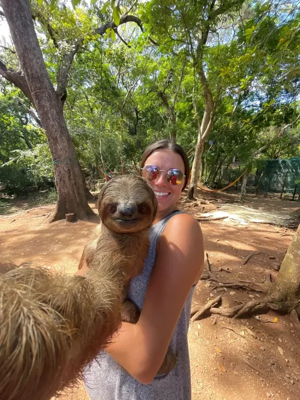 Une femme souriante tient un paresseux dans un environnement tropical