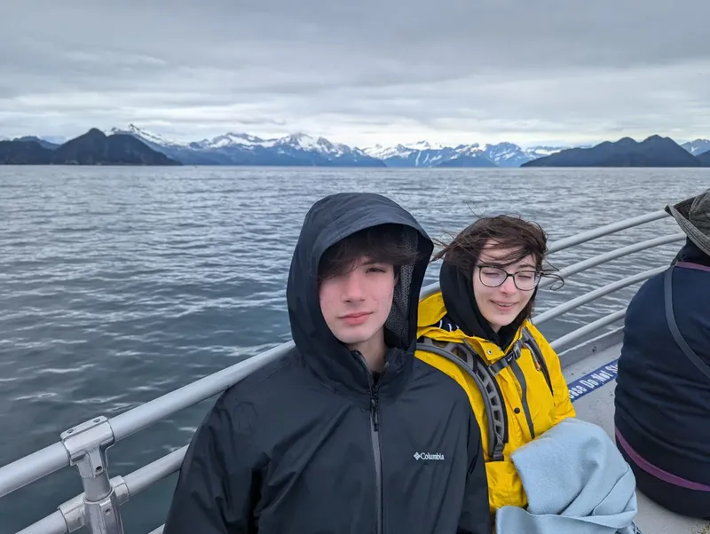 Deux jeunes adultes sur un bateau, regardant un paysage montagneux enneigé