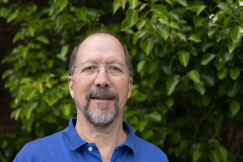 Portrait d'un homme souriant avec des lunettes devant un feuillage vert