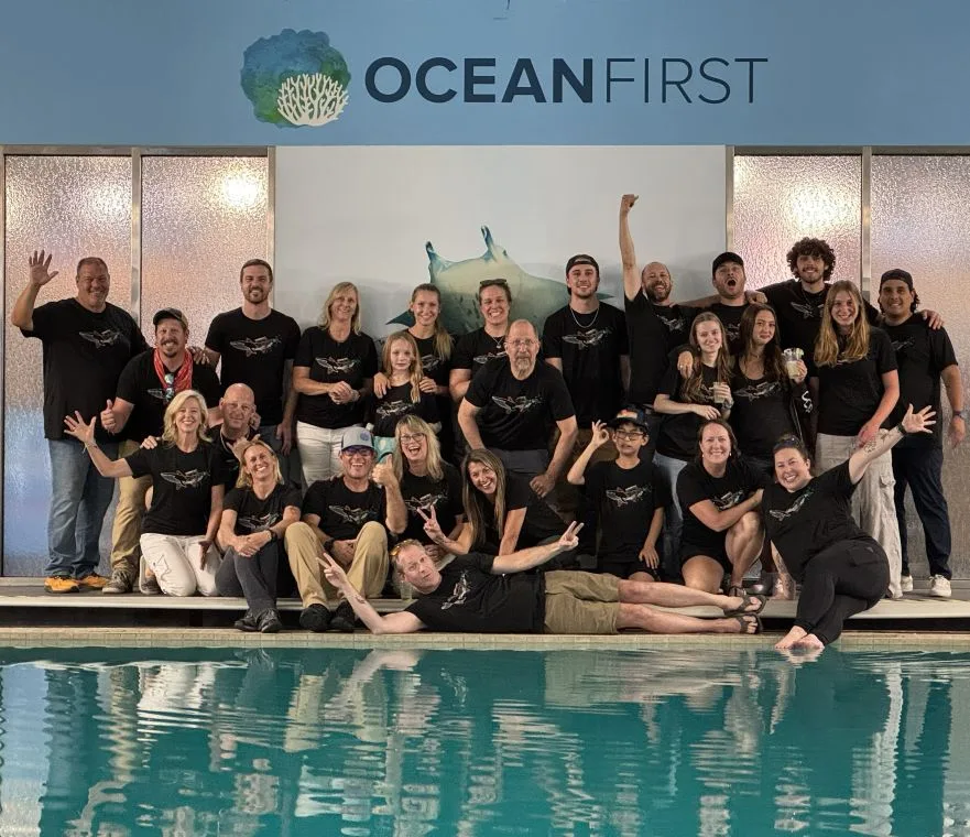 Groupe de personnes souriantes posant devant un mur et une piscine