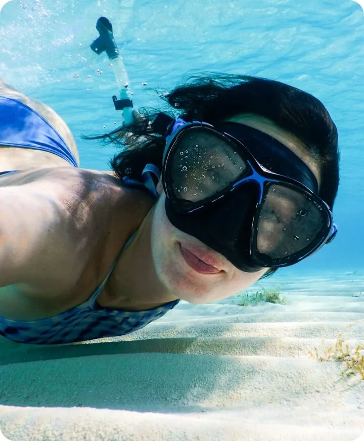Snorkeleuse souriante nageant au-dessus d'un fond sableux clair et turquoise
