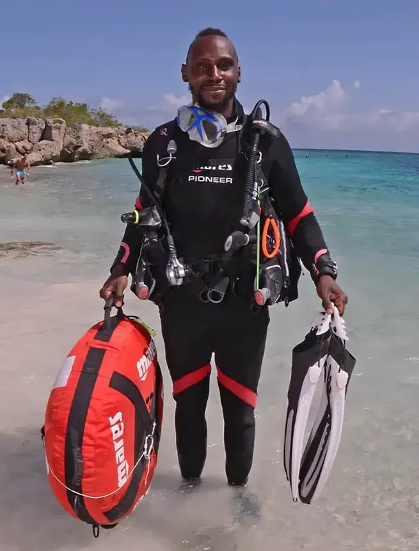 Plongeur équipé sur une plage de sable blanc, regardant la caméra