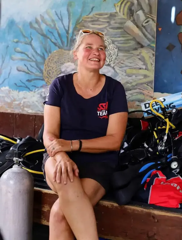 Femme souriante assise devant du matériel de plongée coloré