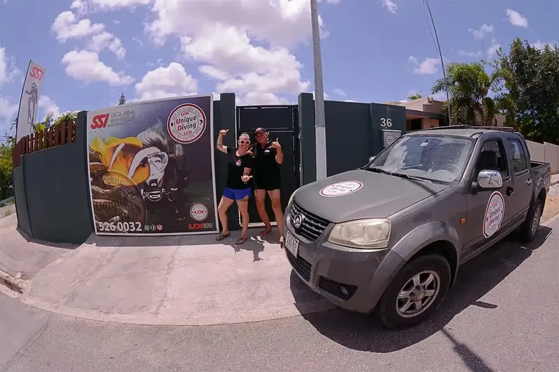Deux personnes souriantes devant un mur avec des affiches de plongée