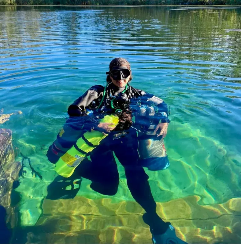 Plongeuse souriante en combinaison, équipée, dans une eau claire et peu profonde