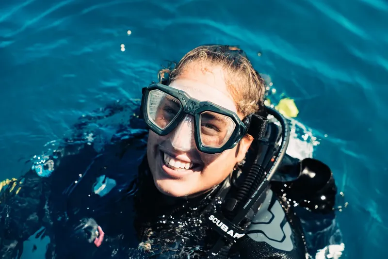 Plongeuse souriante avec masque et détendeur, visage au-dessus de l'eau