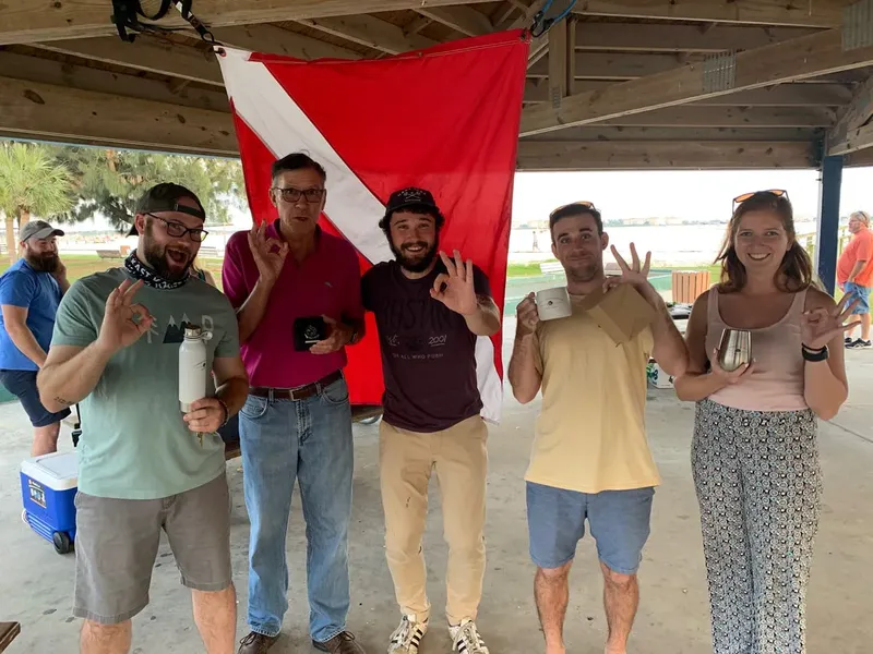 Groupe de personnes souriantes devant un drapeau de plongee rouge et blanc