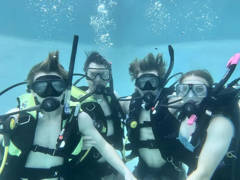 Quatre plongeurs souriants, équipés, flottent dans une eau turquoise claire