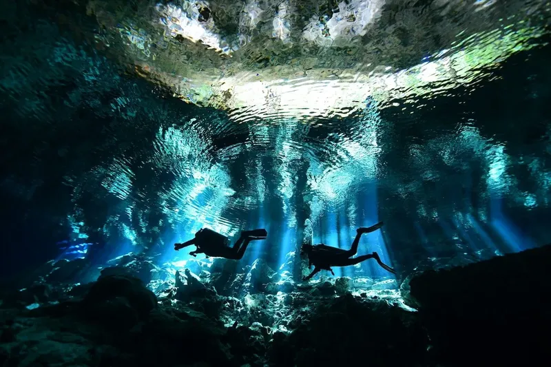 Deux plongeurs explorent une grotte sous-marine éclairée par des rayons de soleil