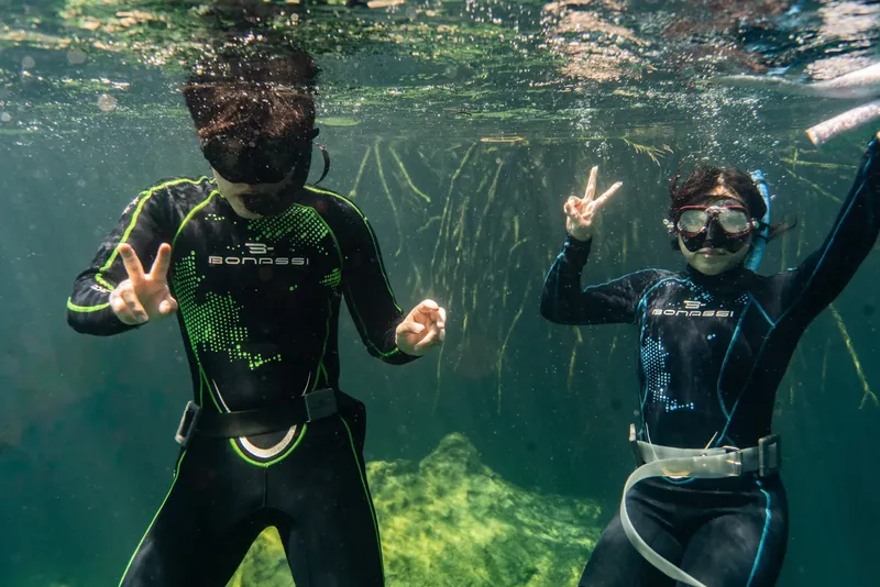 Deux plongeurs sourient et font des signes de la main sous l'eau