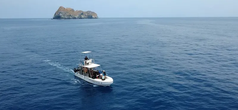 Bateau de plongée navigue en mer vers une île rocheuse lointaine
