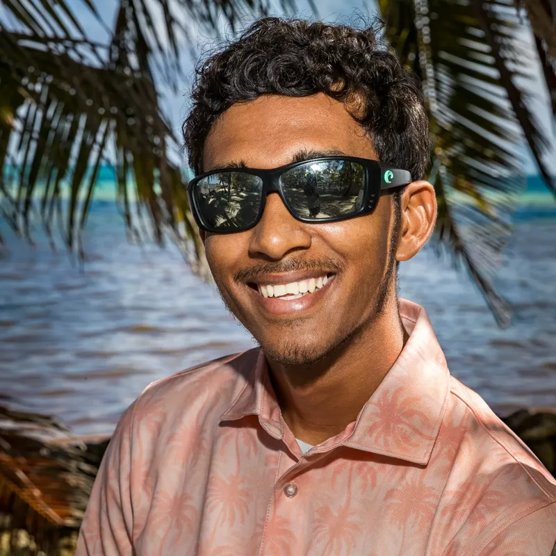 Jeune homme souriant portant des lunettes de soleil sur fond tropical