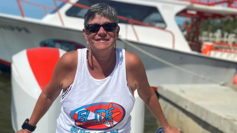 Femme souriante avec débardeur portant un logo devant un bateau