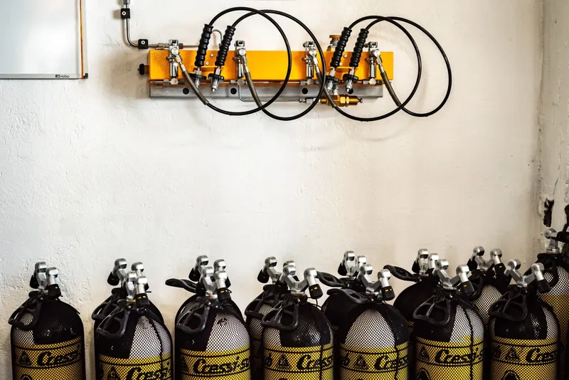 Rangée de bouteilles de plongée remplies, avec un compresseur mural jaune