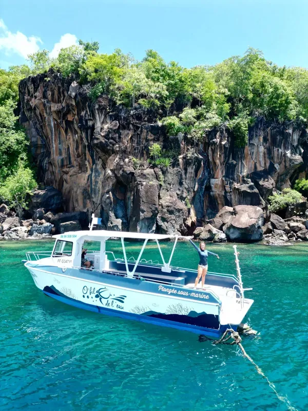Bateau de plongée amarré devant une falaise rocheuse et une plongeuse