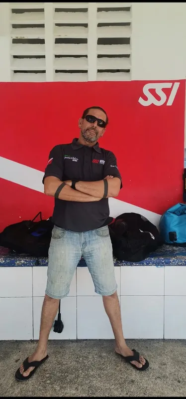 Homme en tenue de plongée, bras croisés, devant un mur rouge