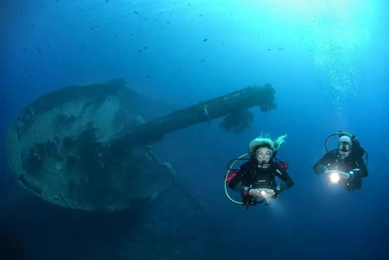 Deux plongeurs explorent une épave sous-marine dans l'eau bleue