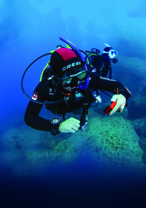 Plongeur en combinaison noire équipé, explorant un récif sous-marin bleu