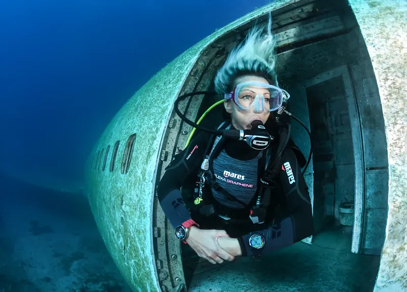 Plongeuse explorant l'épave d'un avion sous l'eau, visibilité claire