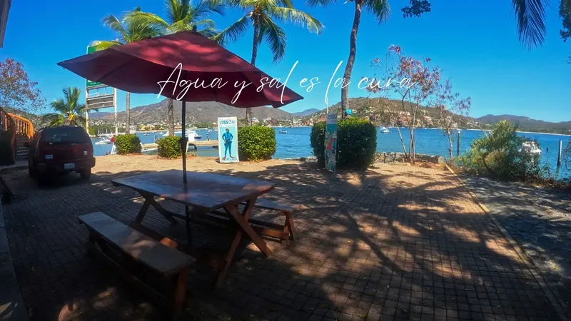 Terrasse avec parasol, tables, bateaux en arrière-plan et texte en espagnol