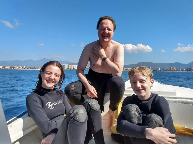 Trois personnes souriantes en combinaison de plongée sur un bateau