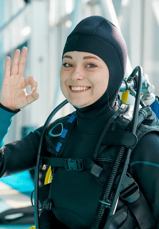 Plongeuse souriante avec combinaison et équipement, geste de validation