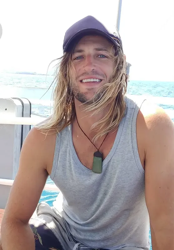 Jeune homme souriant sur un bateau en mer, portant une casquette