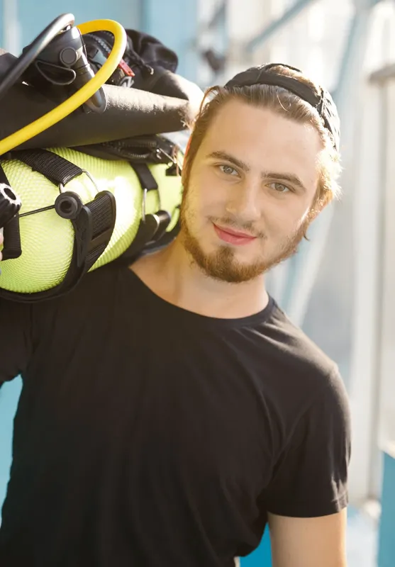 Jeune plongeur souriant portant une bouteille sur son épaule