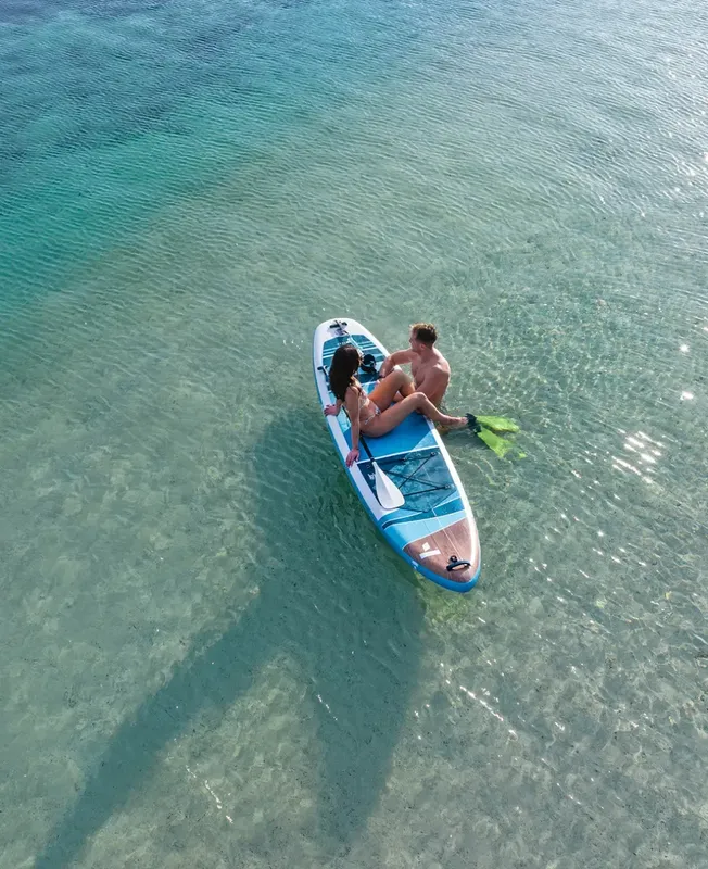 Un couple sur une planche de paddle dans une eau turquoise claire
