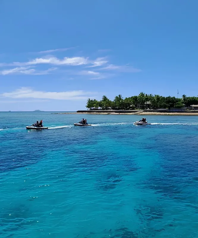 Trois jet-skis naviguent sur une mer turquoise sous un ciel bleu