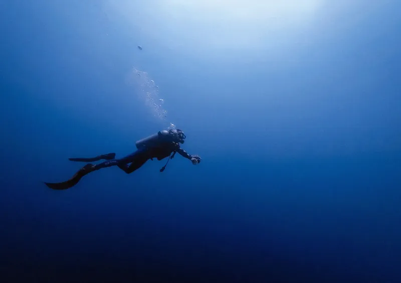 Plongeur en scaphandre nageant dans une eau bleue profonde et claire