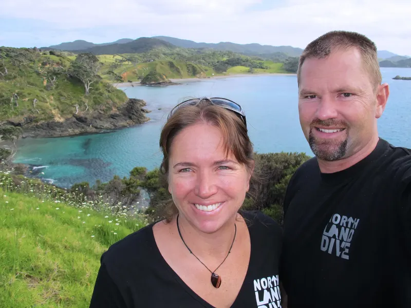 Couple souriant devant une baie verdoyante et une mer turquoise