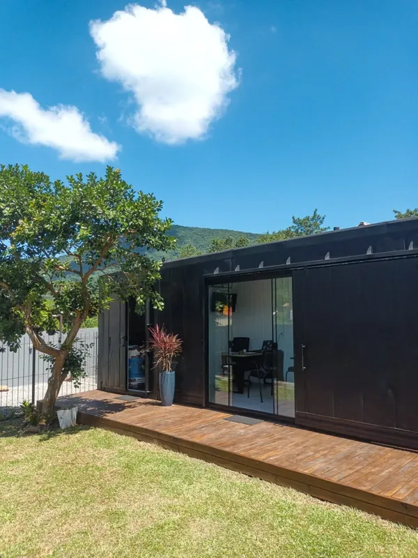 Façade d'un bâtiment noir avec terrasse en bois et végétation luxuriante