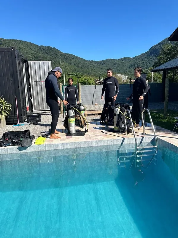 Quatre plongeurs équipés près d'une piscine, préparation matériel plongée