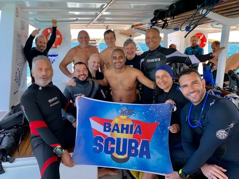 Groupe de plongeurs souriants tenant une bannière colorée sur un bateau