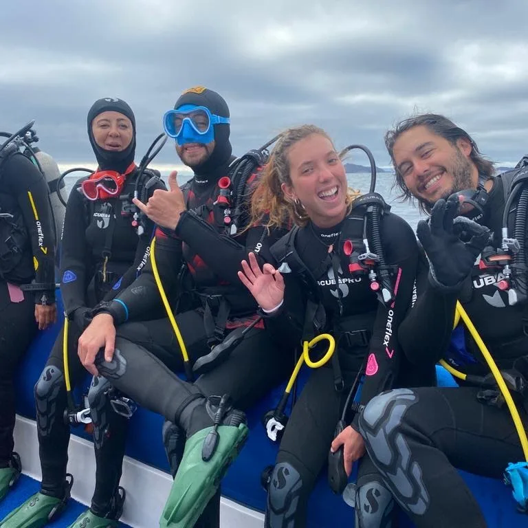 Groupe de plongeurs souriants sur un bateau, équipement complet visible