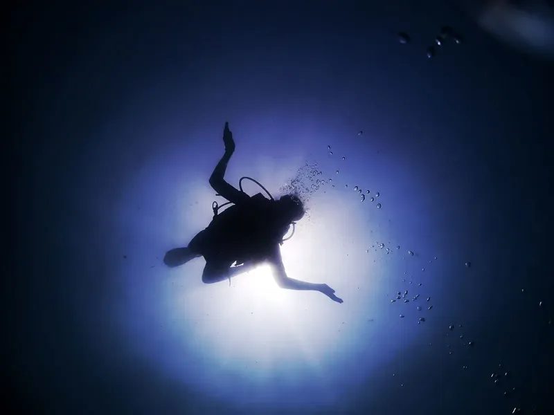 Plongeur silhouetté nageant vers la surface dans l'eau bleue
