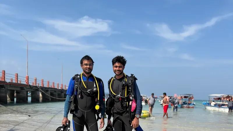 Deux plongeurs souriants en combinaison, équipés, sur un quai ensoleillé