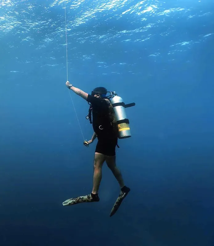 Plongeur en apnée, corps en position verticale, bras levé vers la surface