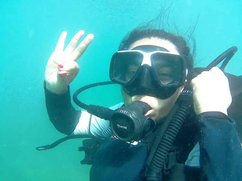 Plongeuse souriante sous l'eau, faisant un signe de la main