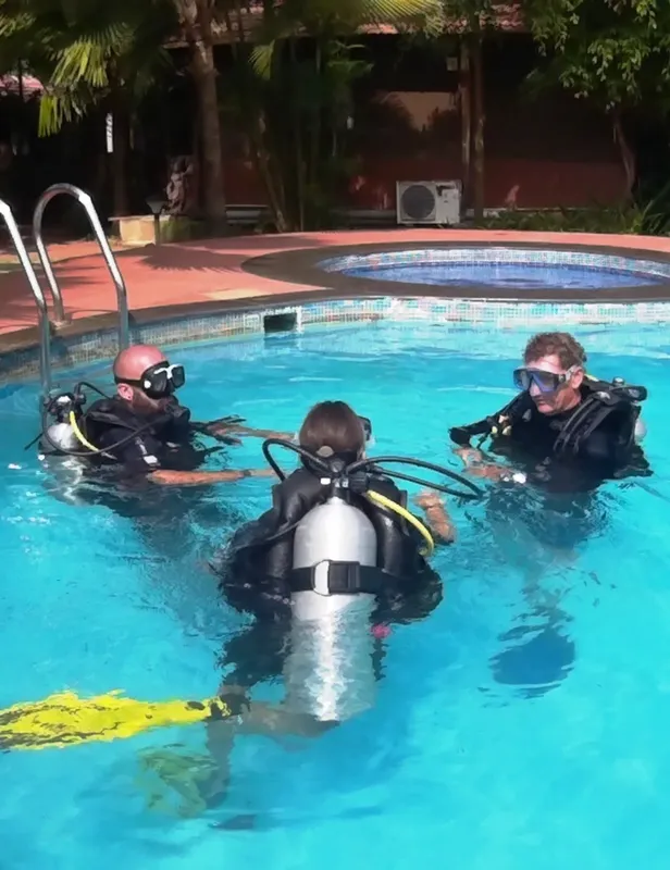 Trois plongeurs en formation dans une piscine, équipement complet visible