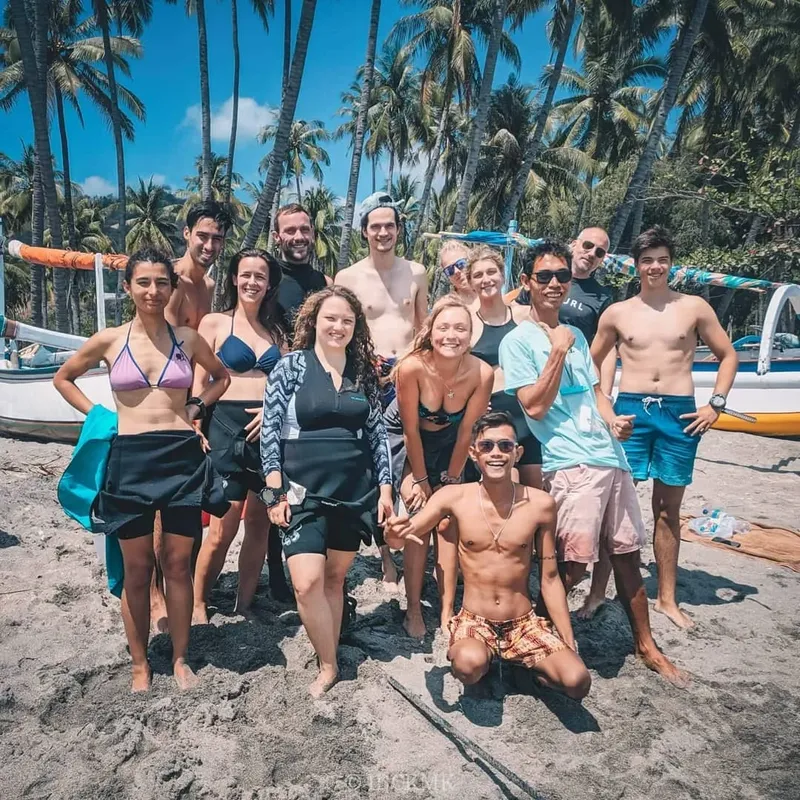 Groupe de personnes souriantes sur une plage avec des bateaux en arrière-plan