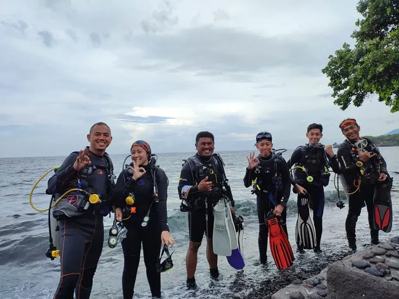 Groupe de plongeurs souriants sur une plage rocheuse, équipement complet